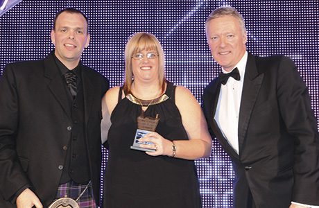 Richard Jones, national account controller of award sponsor Müller Wiseman Dairies, left, and awards event host Rory Bremner, right, present the Scottish Grocer 2015 Dairy Award (Milk) to Angela Pattie of Spar Dalrymple in Ayrshire.