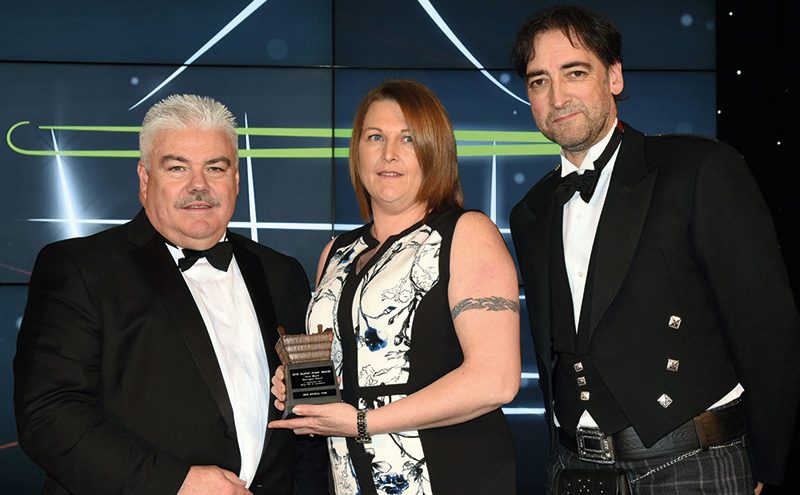 Joe Walker, national accounts manager, Müller Milk & Ingredients, left, and awards event host Alistair McGowan, right, present the Scottish Grocer Dairy Award (managed stores) to Janie Nicholson, Spar Boswell Park.